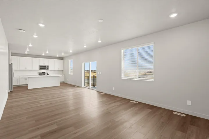 **DISCLAIMER**   Interior package upgrades not photographed. Recessed lighting throughout, wood-finish flooring, white cabinetry, a kitchen island, and a sliding glass door to a balcony