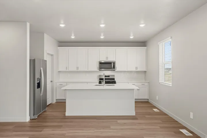 **DISCLAIMER**   Interior package upgrades not photographed. Kitchen featuring white cabinetry, a center island with sink, wood-finish flooring, recessed lighting, and stainless steel appliances