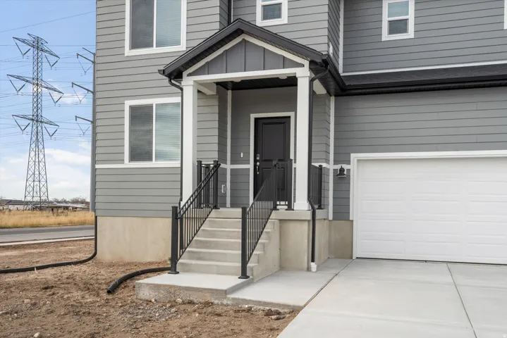 **DISCLAIMER** Elevation may vary.  Gray horizontal siding with white trim, dark entry door, concrete steps with black railings, covered entry porch, and a white garage door