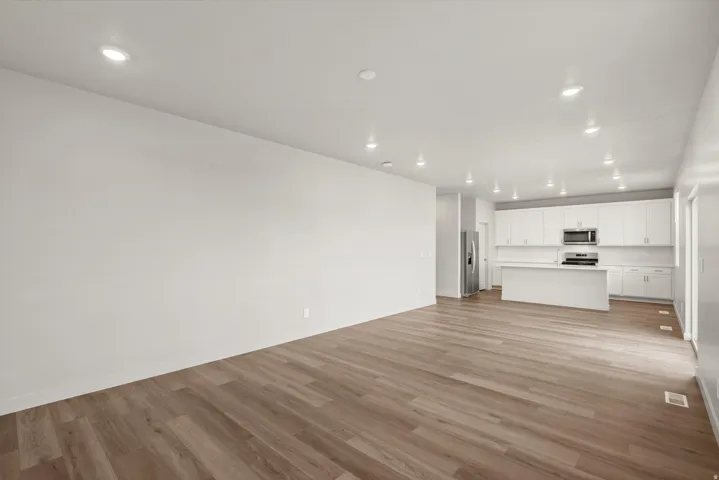 **DISCLAIMER**   Interior package upgrades not photographed. Open-concept living space with wood-finish flooring, recessed lighting, and a kitchen featuring white cabinetry, stainless steel appliances, and a central island