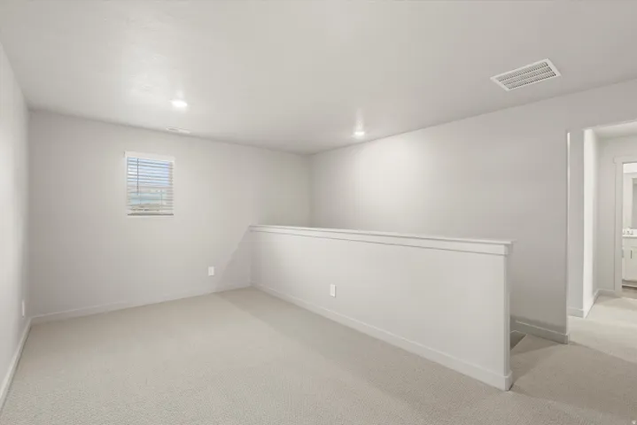 **DISCLAIMER**   Interior package upgrades not photographed. Carpeted open-concept area featuring a window with blinds, recessed lighting, and a partial wall with trim