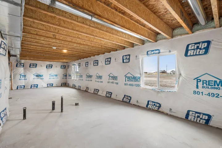 Unfinished basement with exposed wood joists, concrete flooring, and multiple windows