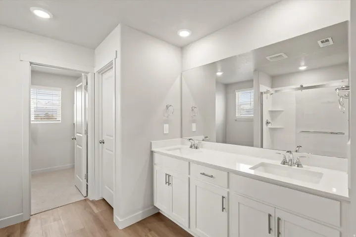**DISCLAIMER**   Interior package upgrades not photographed. Dual vanity with undermount sinks, white cabinetry, a large wall-mounted mirror, and wood-finish flooring