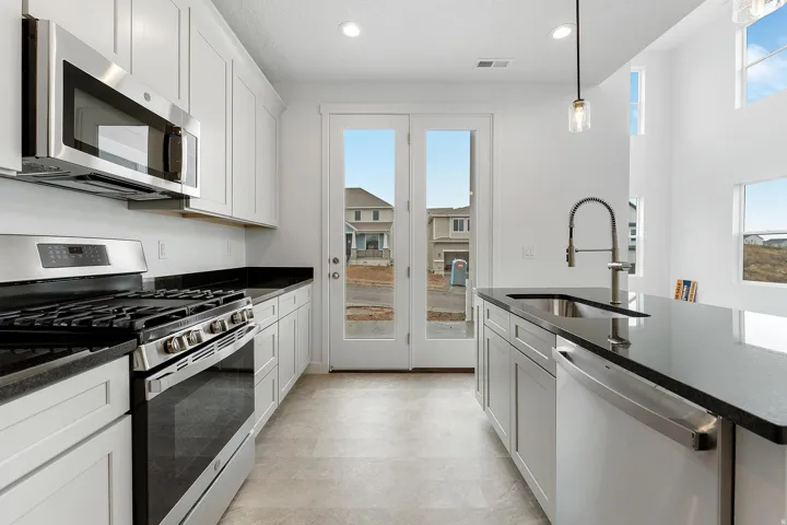 Galley kitchen with white shaker cabinetry, stainless steel appliances, dark countertops, and light-toned flooring