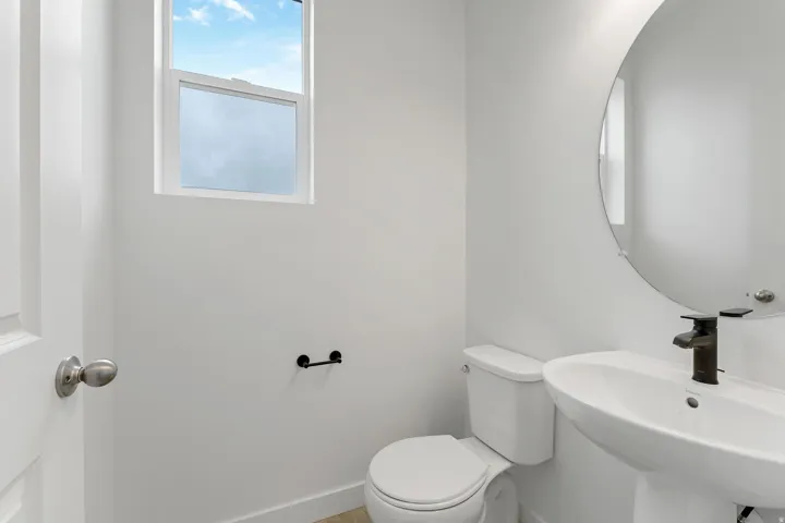 Bright, spa-inspired bathroom featuring a curved mirror with integrated lighting, white ceramic vessel sink with matte black faucet, white porcelain toilet, and light wood-finish flooring