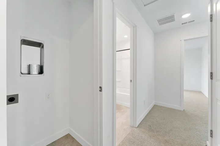 Modern hallway with clean white walls, recessed ceiling lighting, and neutral wood-finish flooring