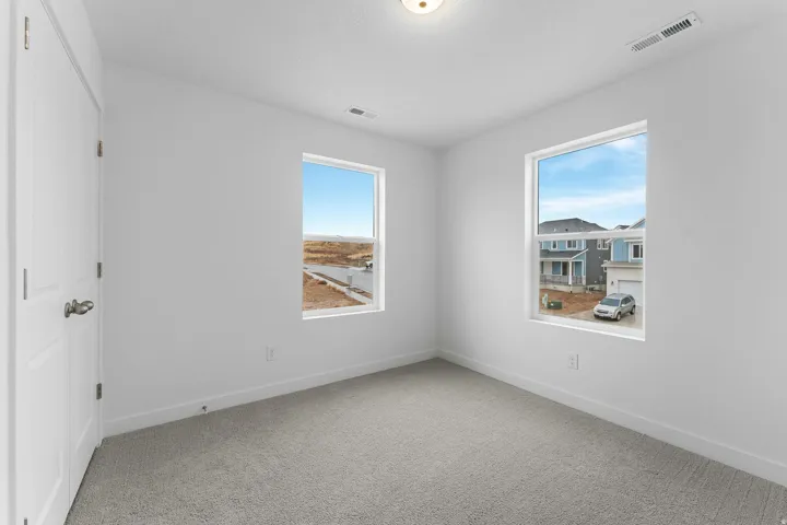 Bright, light-filled bedroom featuring dual windows with expansive natural light, neutral carpet flooring, and clean white walls with recessed ceiling lighting