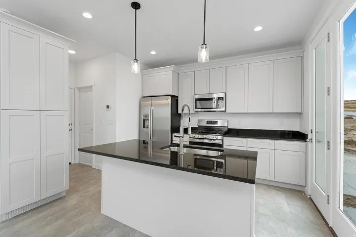 Kitchen featuring white shaker-style cabinetry, dark countertops, stainless steel appliances, a central island, and pendant lighting