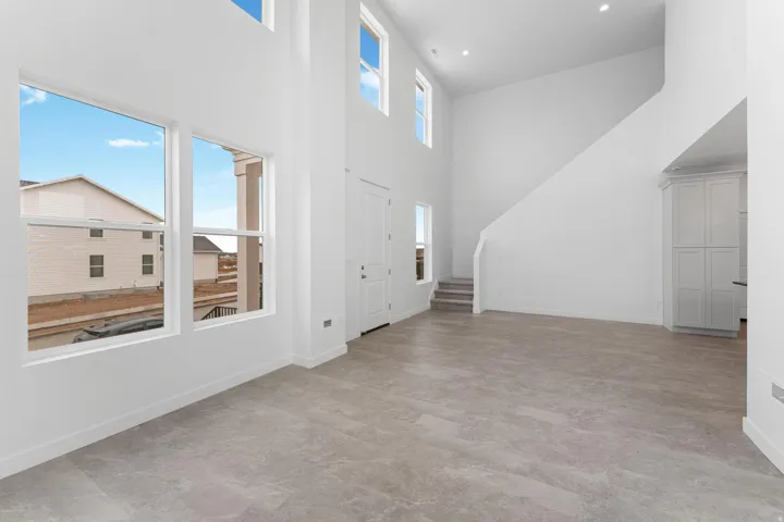 Soaring two-story great room with abundant natural light from expansive windows and clerestory skylights, polished concrete flooring, and a curved staircase with metal railings