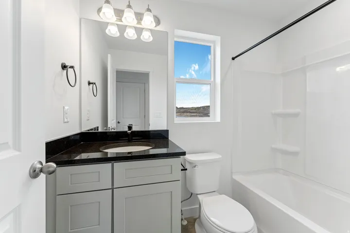 Vanity with dark countertop and undermount sink, built-in tub with shower, and double-hung window