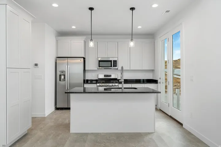 Well-appointed kitchen featuring light-toned cabinetry, stainless steel appliances, a center island with a sink, and pendant lighting