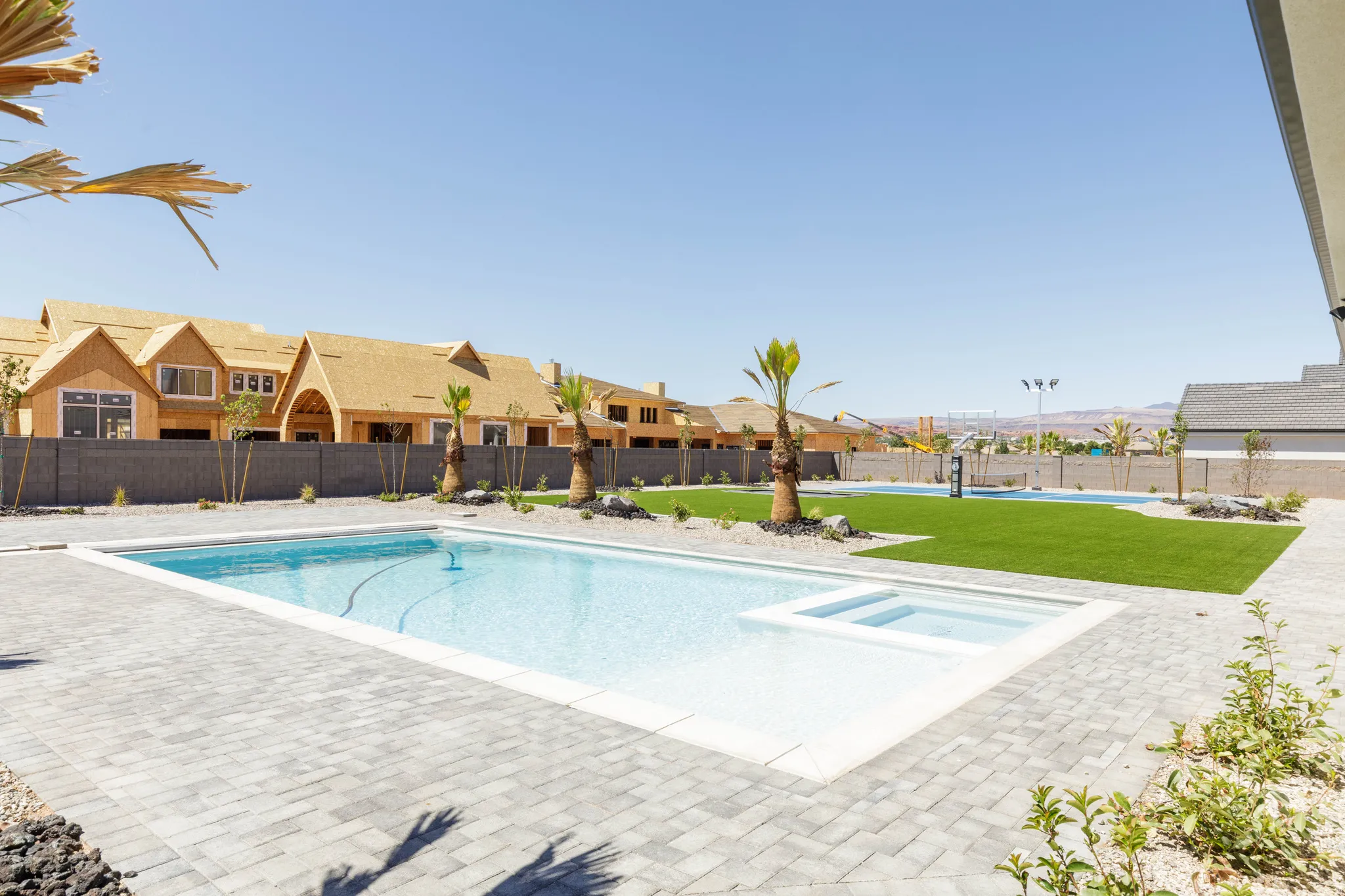 Resort-style backyard featuring a swimming pool, integrated spa, paver patio, and artificial turf lawn