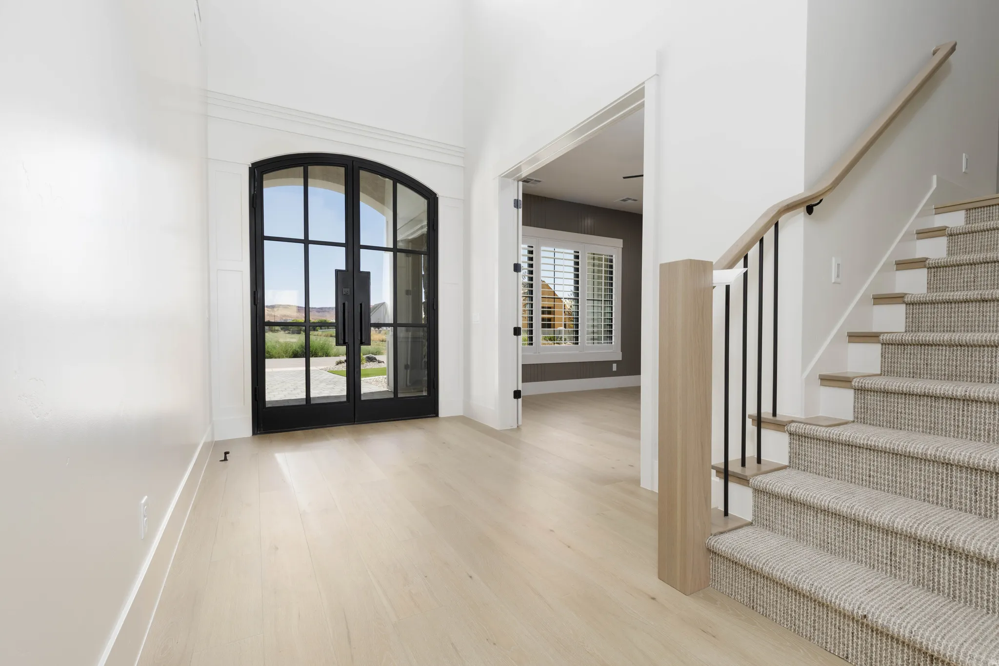 Arched double entry doors, wood-finish flooring, staircase with carpet runner, wood handrail, and wrought iron balusters