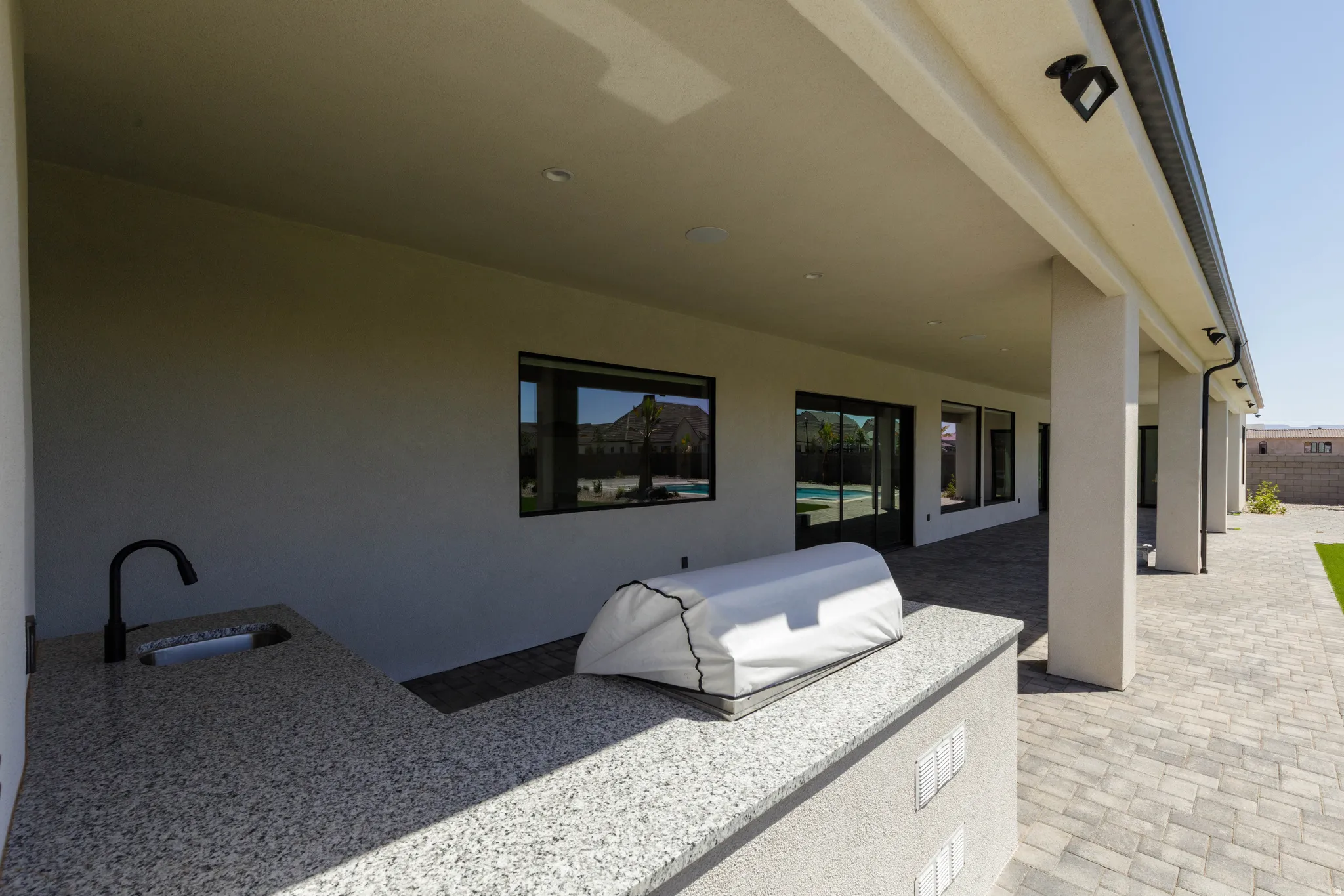 Covered outdoor kitchen area featuring granite countertops, integrated sink with black gooseneck faucet, and recessed lighting