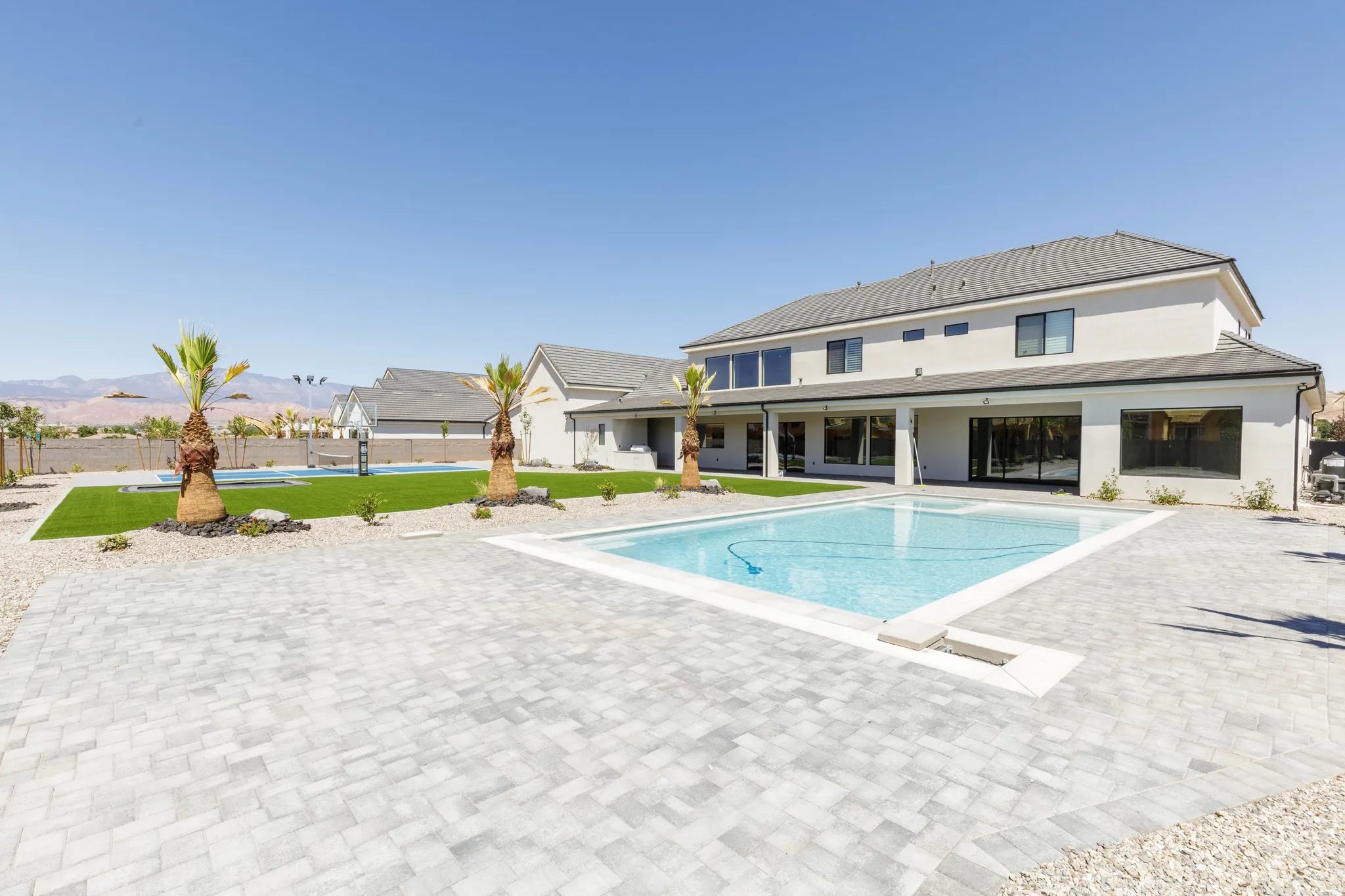 Expansive backyard featuring a large swimming pool, paver patio, artificial turf, and mature palm trees