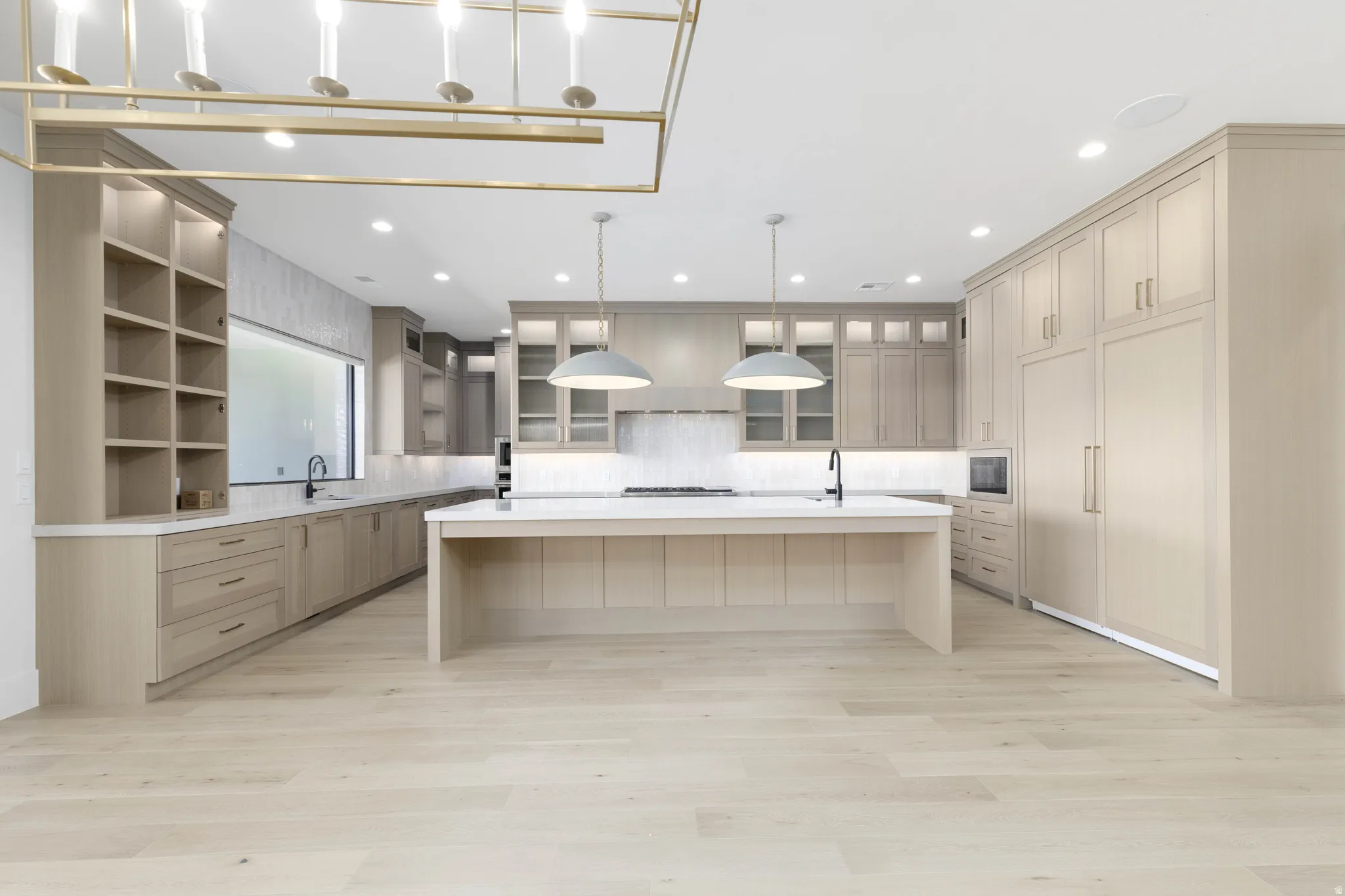 Light wood-finish flooring with a generously sized kitchen island, extensive built-in cabinetry, integrated appliances, and recessed lighting
