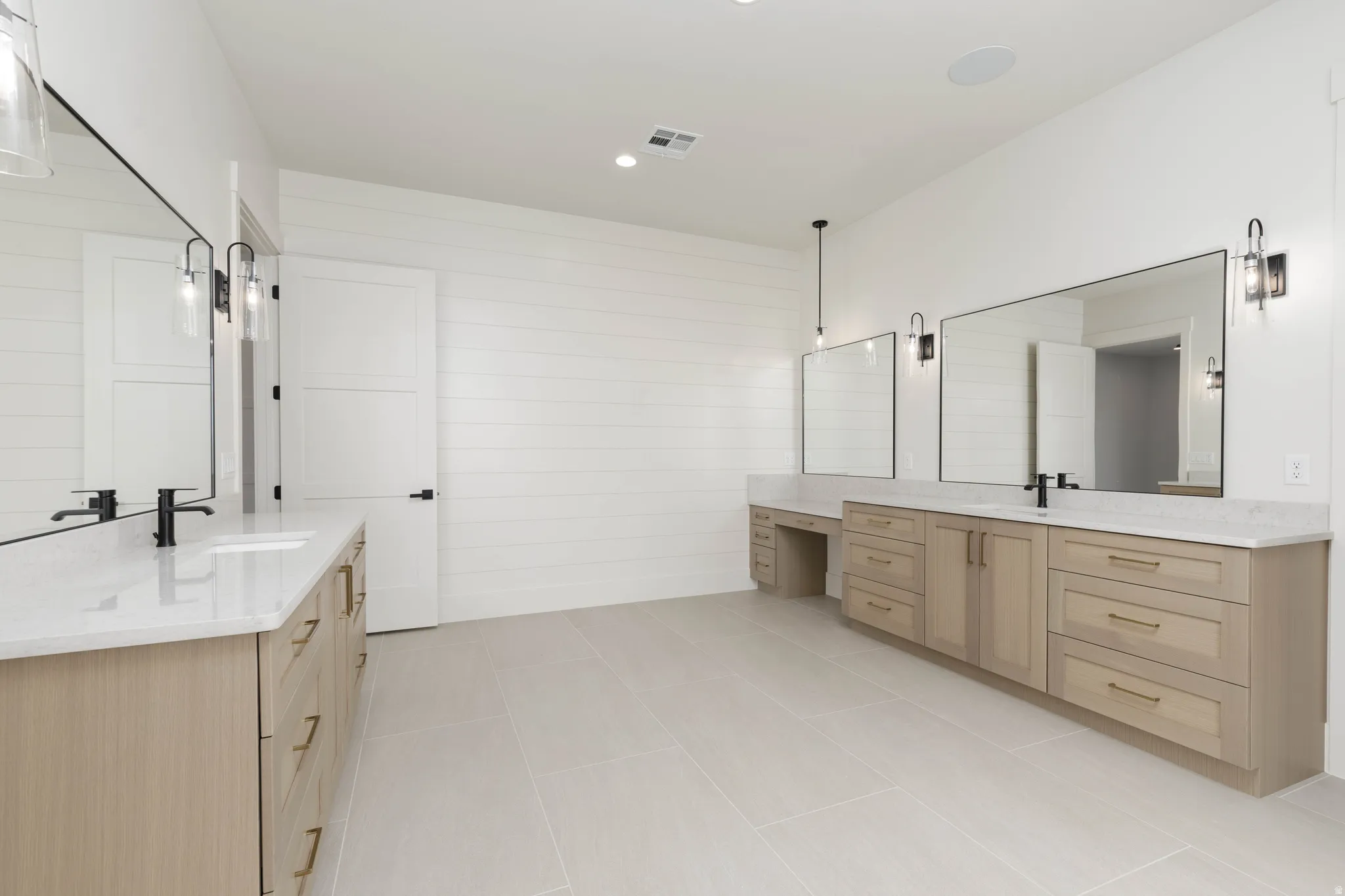 Dual vanities with integrated sinks, light wood-finish cabinetry, quartz countertops, and large framed mirrors