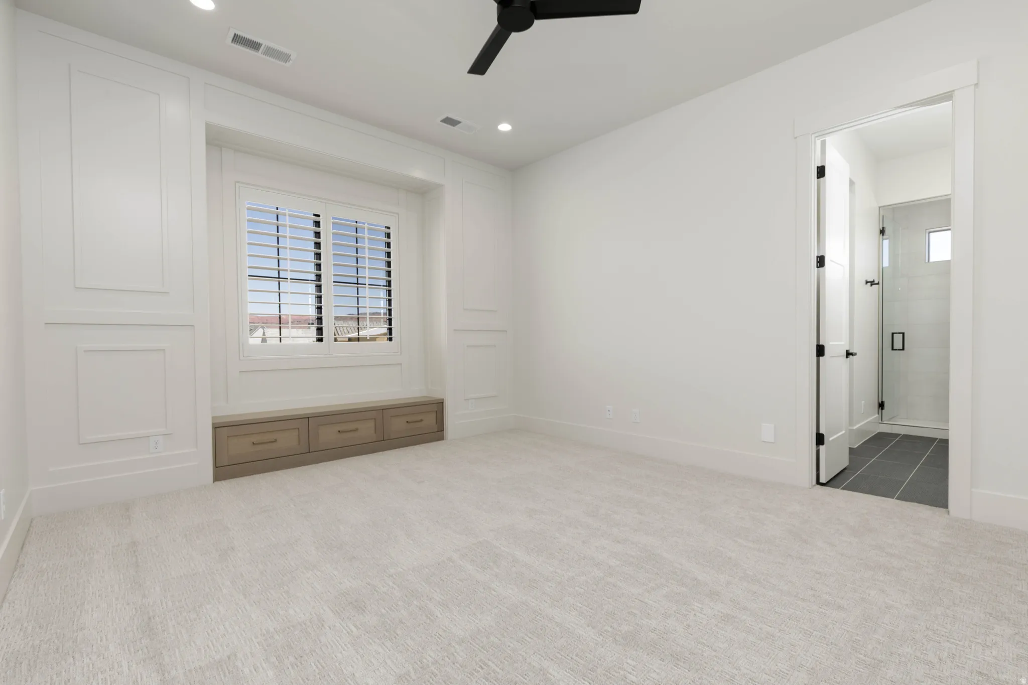 Recessed lighting, ceiling fan, built-in window seat with storage drawers, plantation shutters, and a glass-enclosed shower with tiled walls