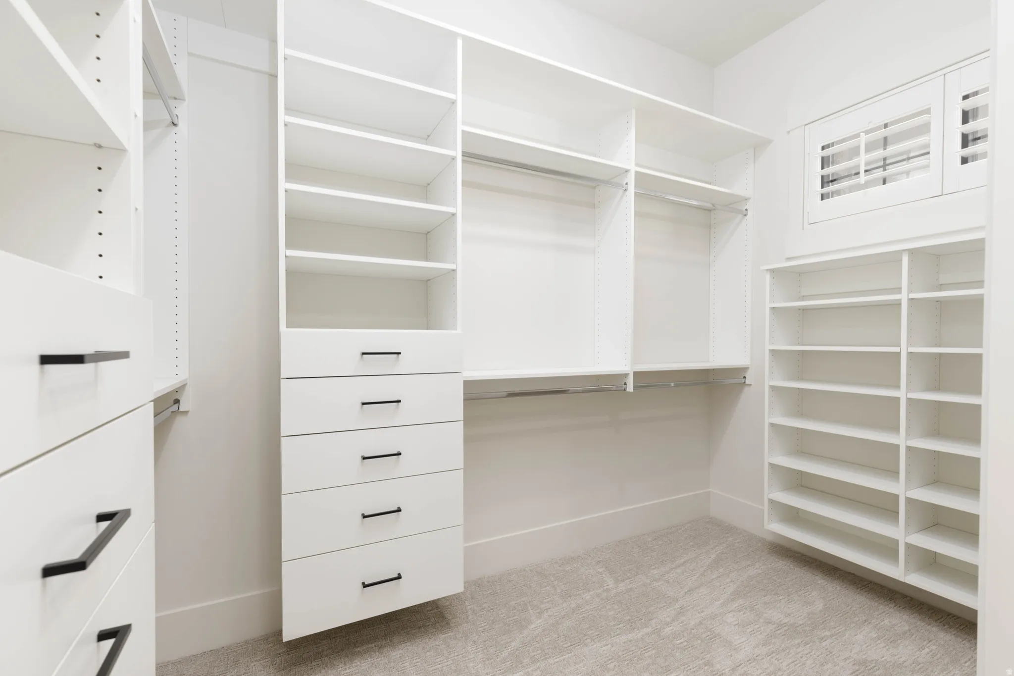 Custom closet system featuring multiple shelves, hanging rods, built-in drawers with black hardware, and an integrated window with shutters