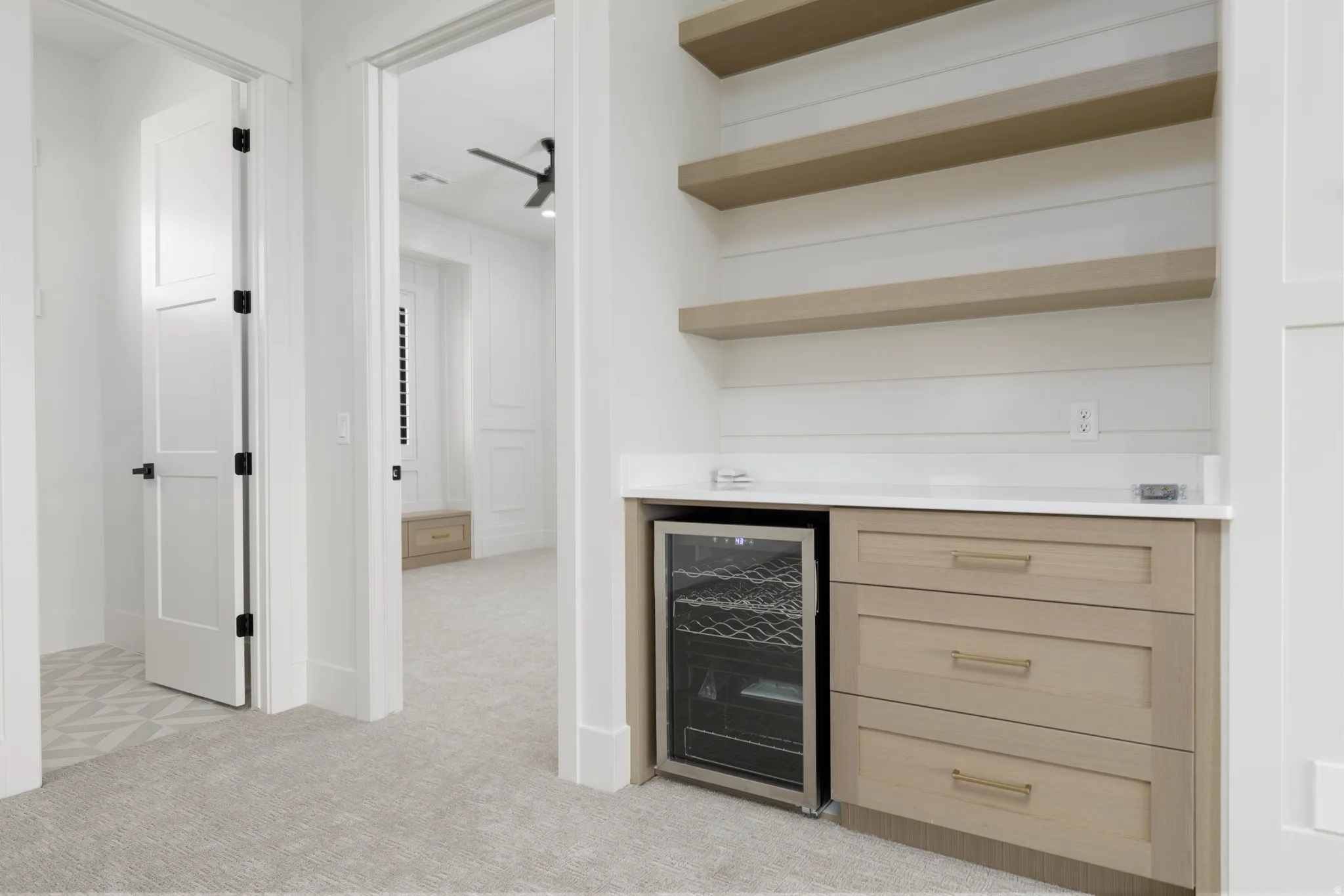 Built-in refreshment bar featuring a wine refrigerator, open shelving, wood-finish cabinetry, and a light-toned countertop