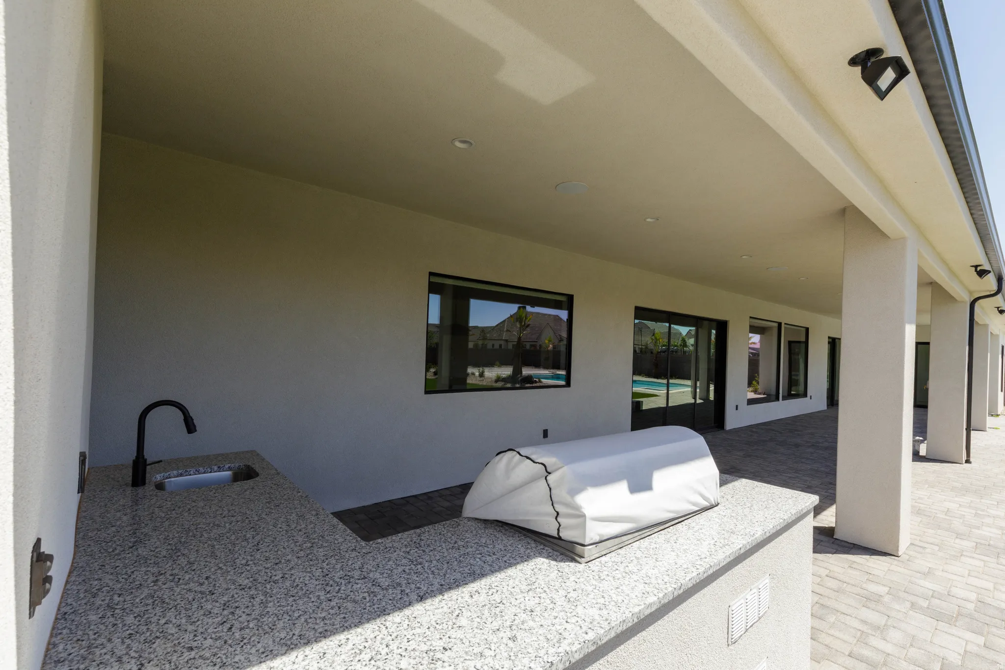 Covered patio featuring an outdoor kitchen with a built-in sink and granite-finish countertop, recessed lighting, and patio pavers