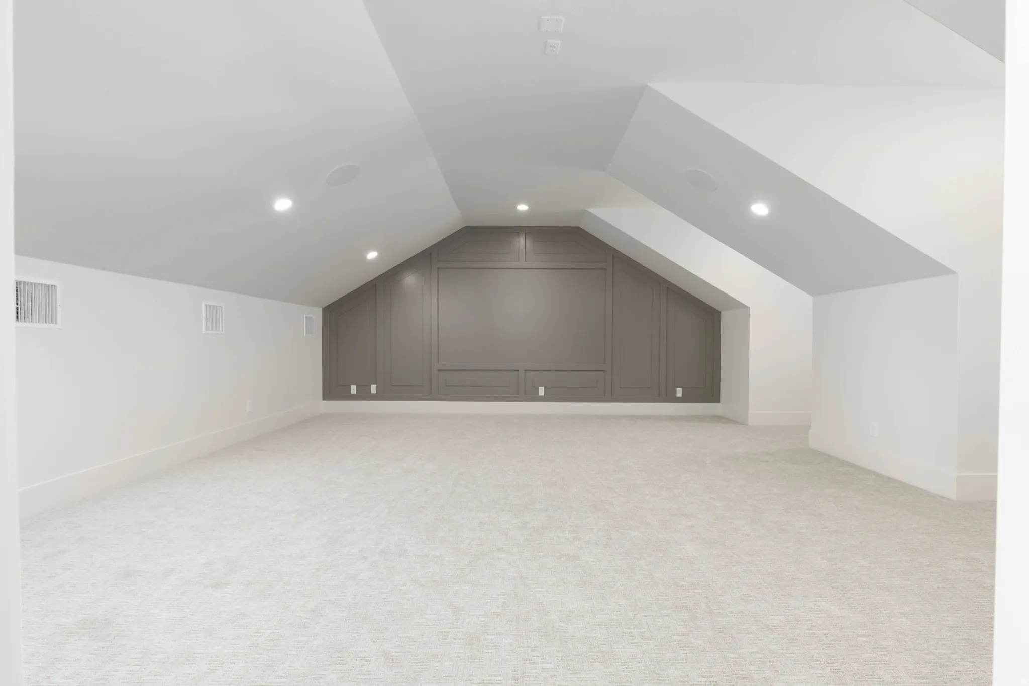 Sloped ceiling design with recessed lighting, integrated wall paneling, and light-toned carpeting