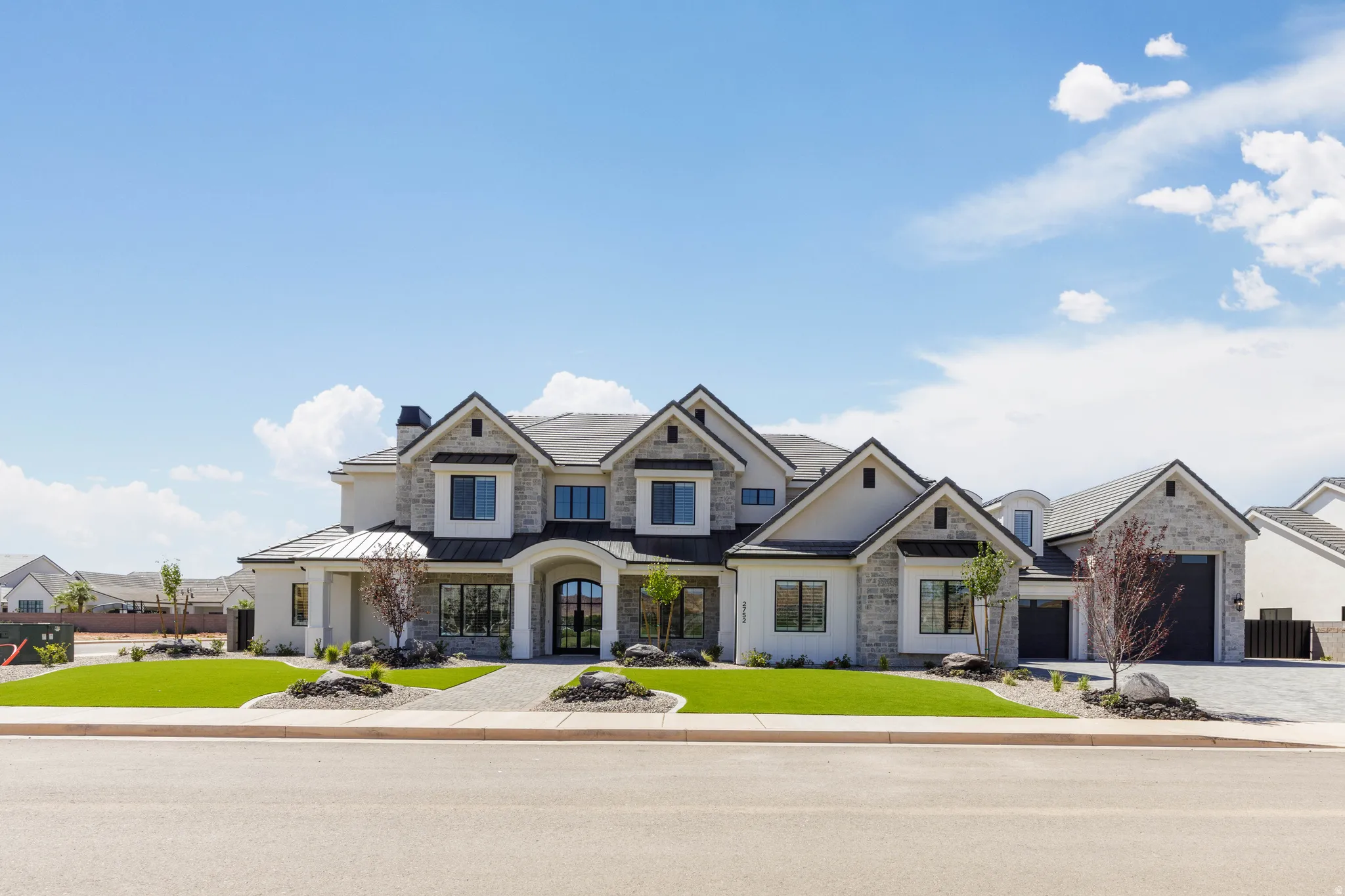 Contemporary exterior featuring a light-colored stucco finish, stone accents, multiple gables, a dark roof, and an arched entry