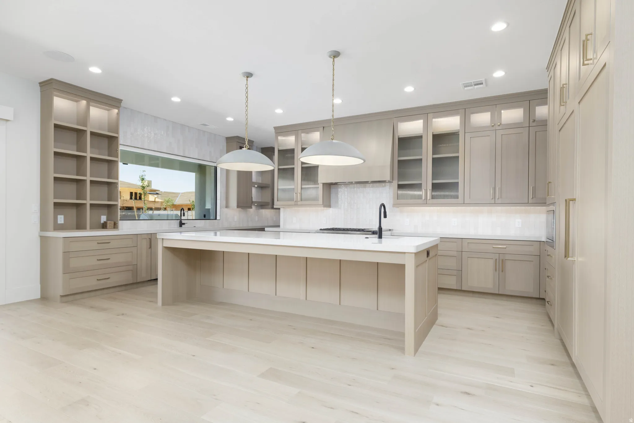 Kitchen featuring extensive light wood-tone cabinetry, a central island with a white countertop and sink, light wood-finish flooring, a linear window above the sink, and recessed ceiling lighting