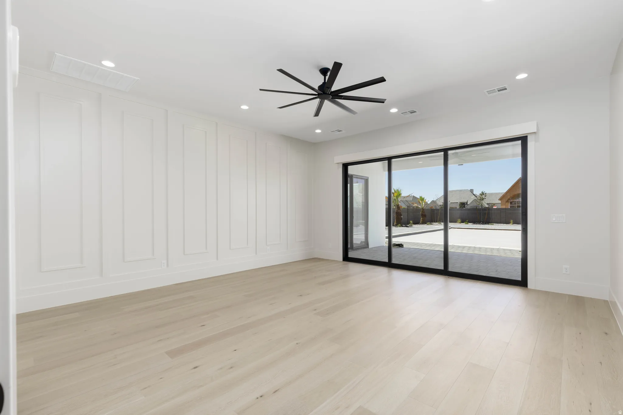 Wood-finish flooring, accent panel wall, recessed lighting, ceiling fan, and large sliding glass doors