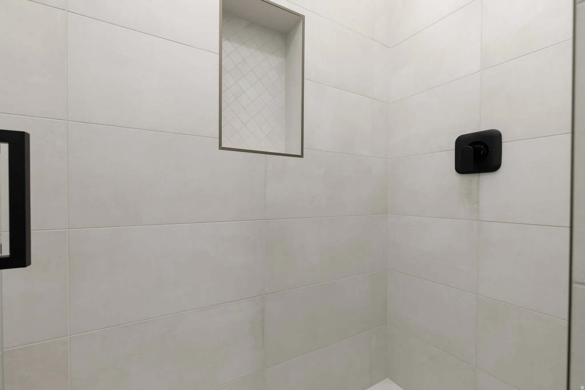 Tiled shower enclosure featuring a built-in niche with diamond pattern accent tile, and a matte black shower control