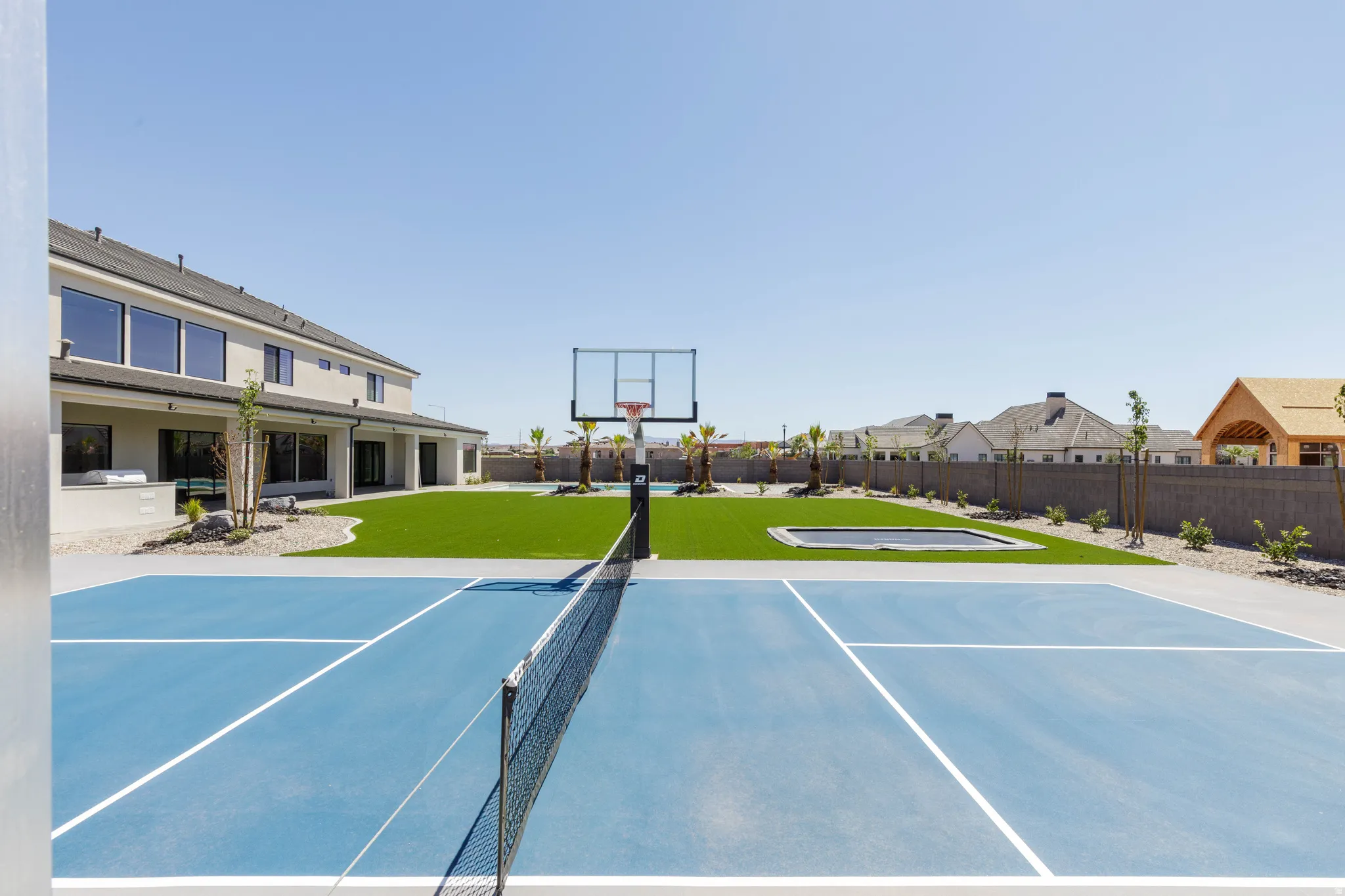 Multi-sport court, artificial turf lawn, basketball hoop, built-in trampoline, and stucco exterior
