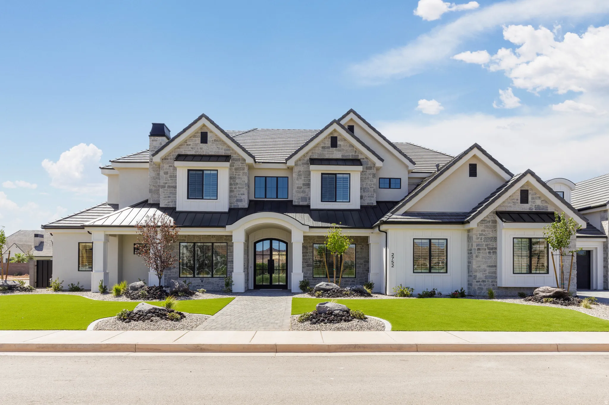 Multi-gabled exterior featuring stone and stucco finishes, a covered arched entry, black-framed windows, and a paver pathway