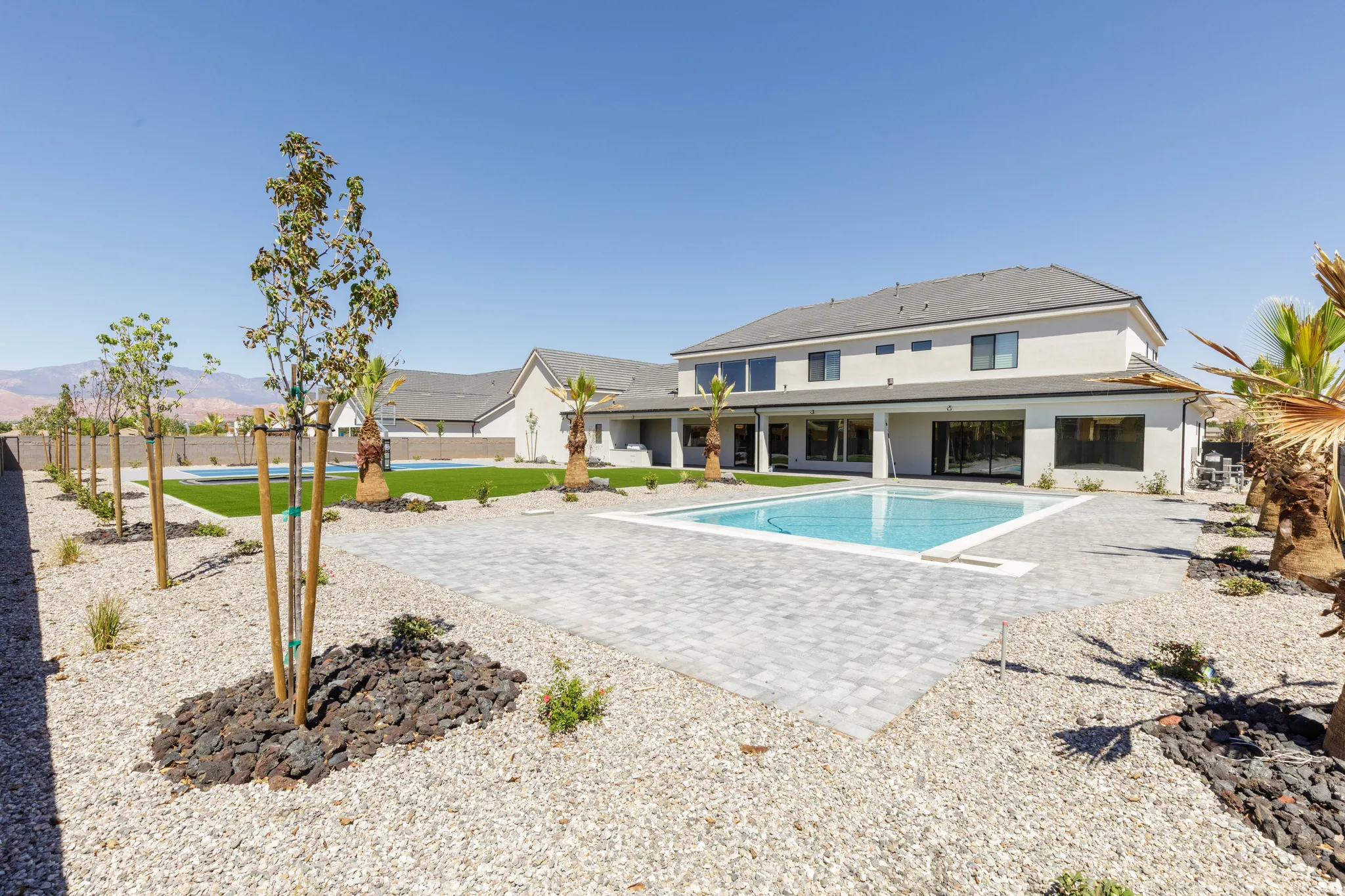 Expansive outdoor space featuring a swimming pool with a paved surround, a manicured lawn area, and mature palm trees