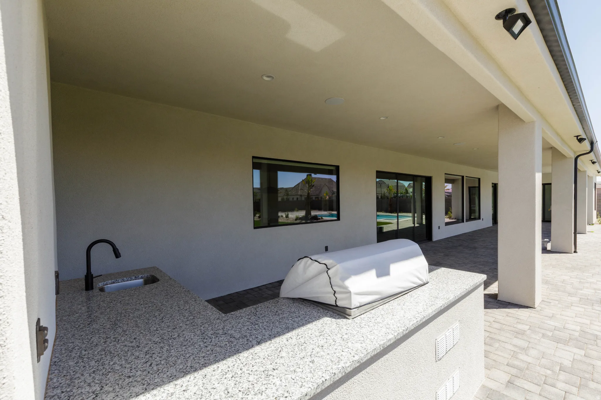 Expansive covered patio featuring a built-in outdoor kitchen with a sink and a counter, and a paved surface