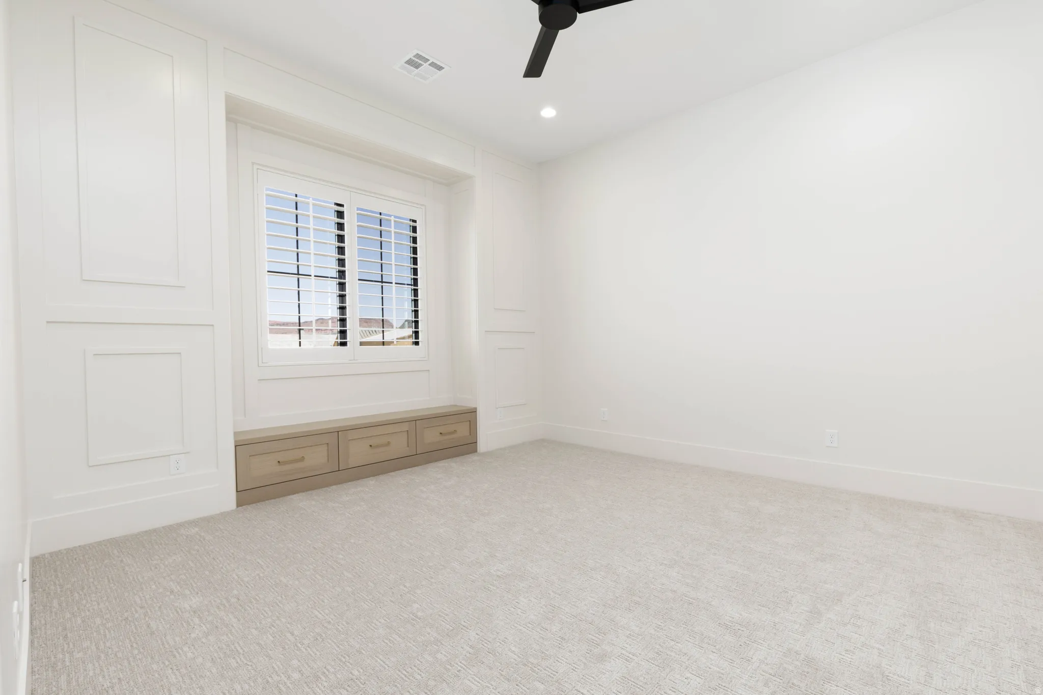 Built-in window seat with storage, custom millwork wall paneling, plantation shutters, recessed lighting, and a ceiling fan