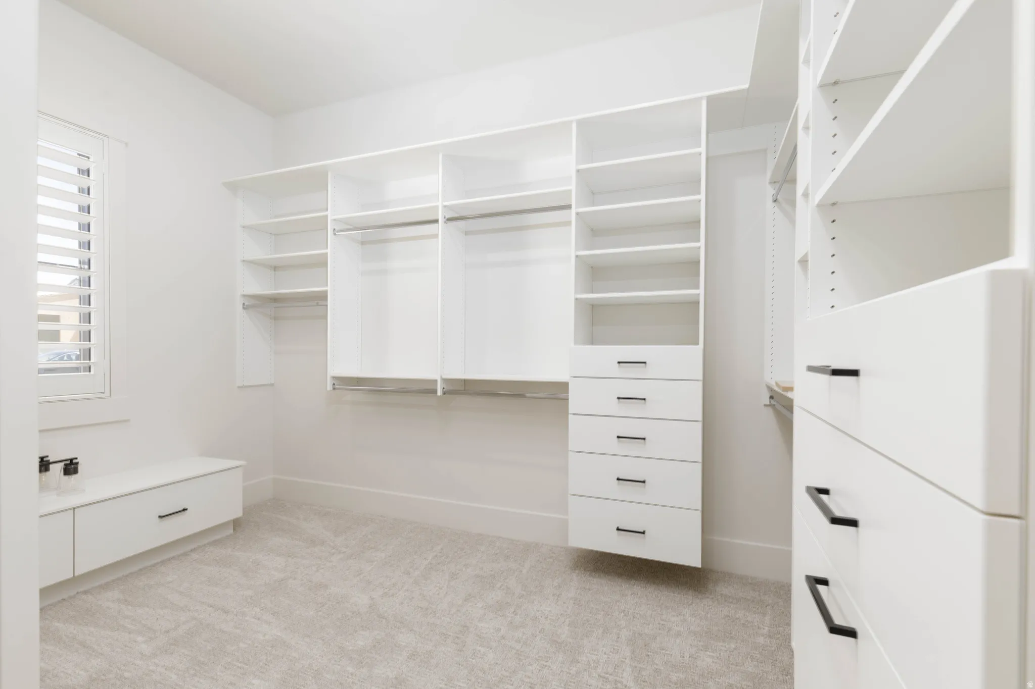 Expansive custom closet system with white cabinetry, integrated shelving, hanging rods, and multiple drawers featuring dark pull hardware