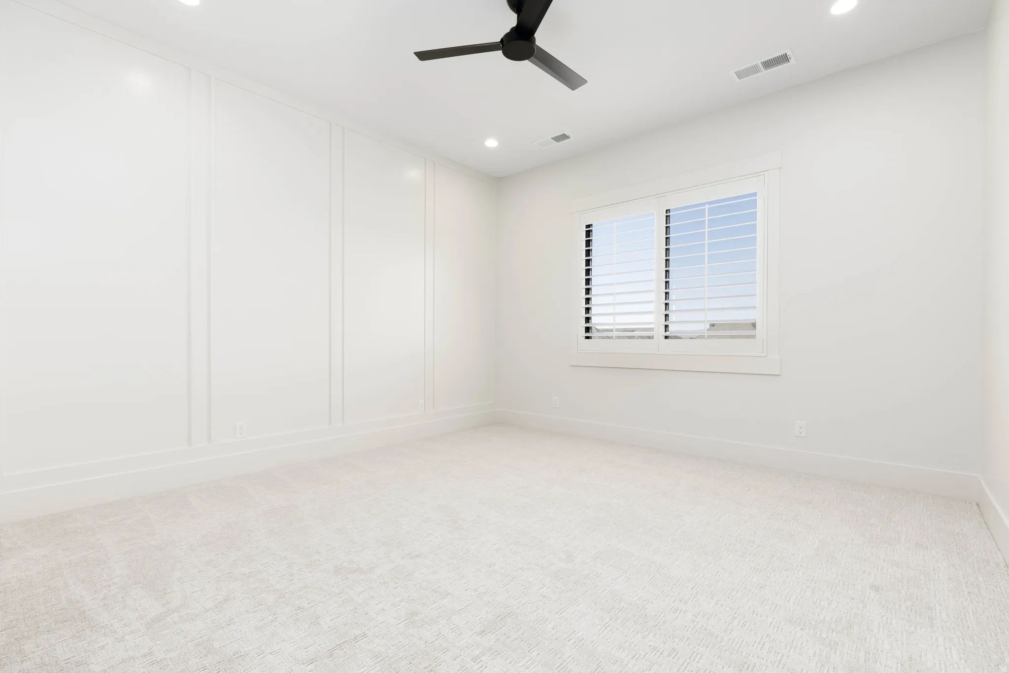 Recessed lighting, ceiling fan, window with plantation shutters, wainscoting, and carpet flooring