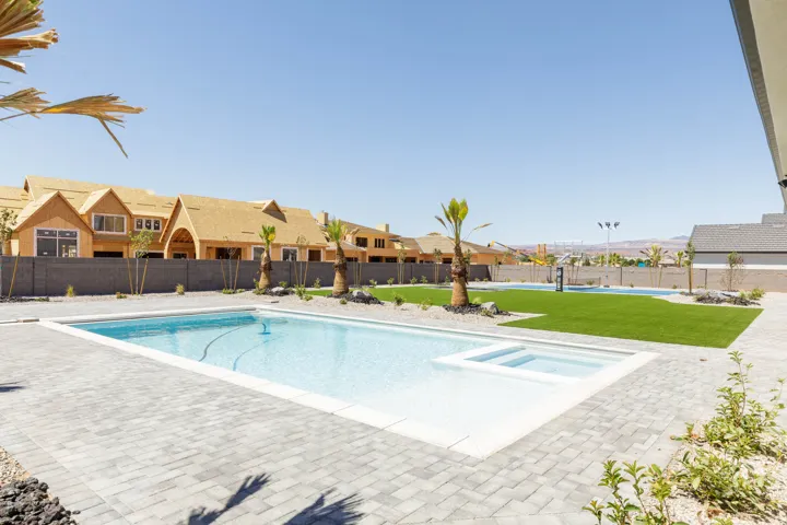 Resort-style backyard featuring a swimming pool, integrated spa, paver patio, and artificial turf lawn