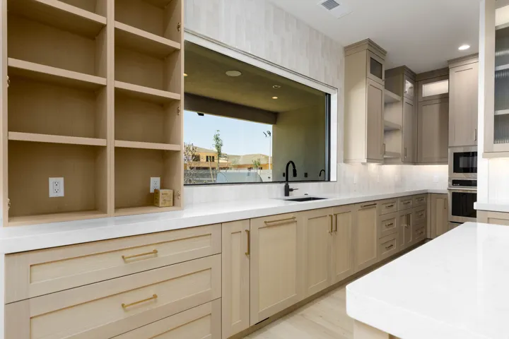 Sleek kitchen featuring light wood-finish cabinetry, white countertops, built-in shelving, a large horizontal window, and integrated appliances