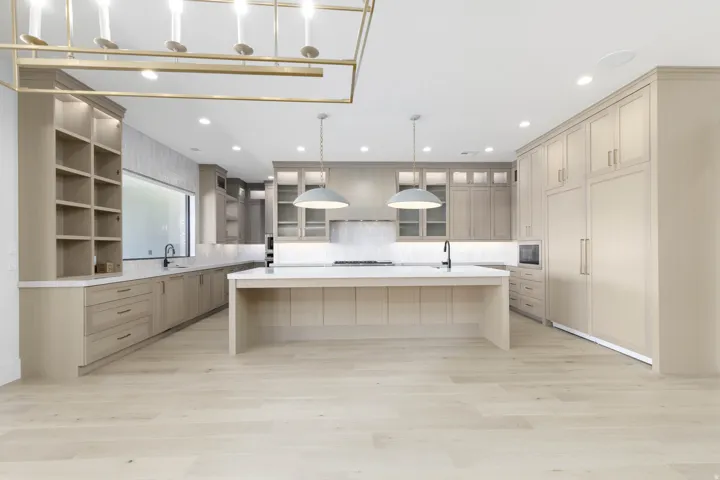 Light wood-finish flooring with a generously sized kitchen island, extensive built-in cabinetry, integrated appliances, and recessed lighting