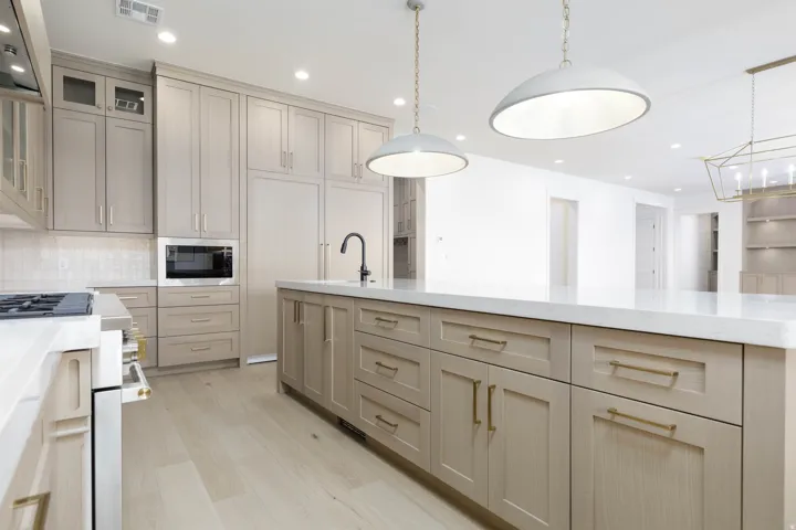 Spacious kitchen featuring an expansive central island, light wood-finish flooring, abundant light-toned cabinetry, recessed and pendant lighting, and a built-in microwave