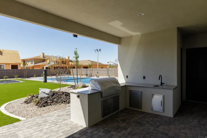 Covered patio with paver flooring, built-in outdoor kitchen with sink, artificial turf lawn, and a pool