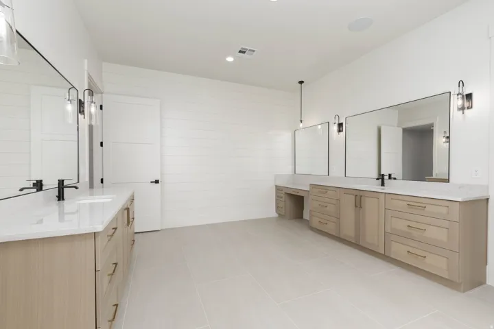 Dual vanities with integrated sinks, light wood-finish cabinetry, quartz countertops, and large framed mirrors