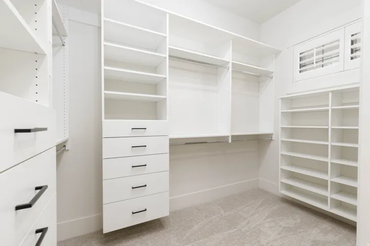 Custom closet system featuring multiple shelves, hanging rods, built-in drawers with black hardware, and an integrated window with shutters