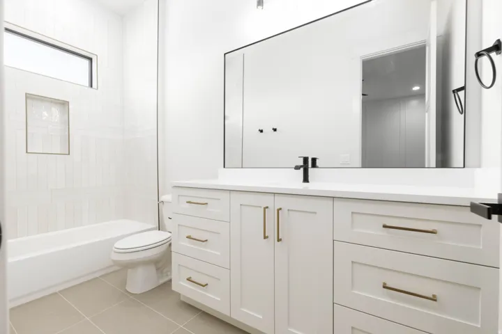 White vanity with bronze hardware, a contrasting black faucet, and a large mirror
