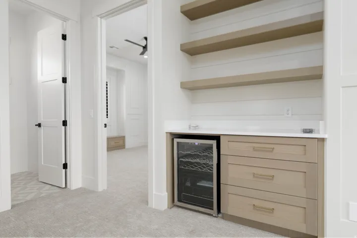 Built-in refreshment bar featuring a wine refrigerator, open shelving, wood-finish cabinetry, and a light-toned countertop