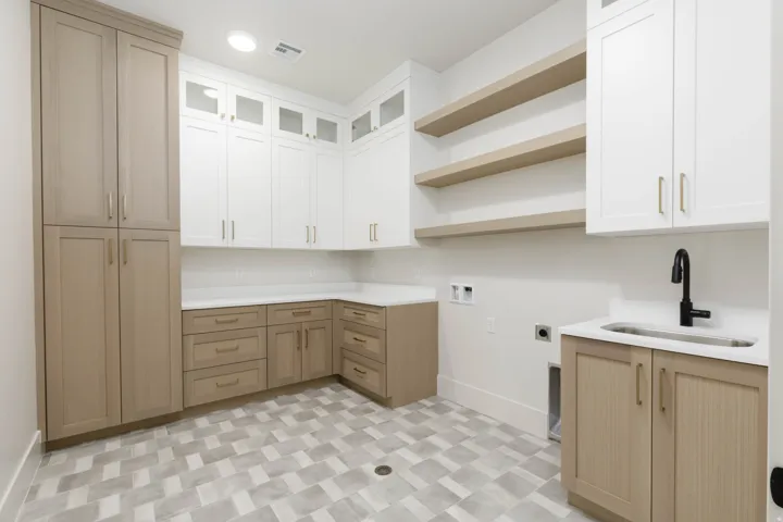 Integrated laundry area featuring varied cabinetry, open shelving, a utility sink with a matte black faucet, and patterned tile flooring