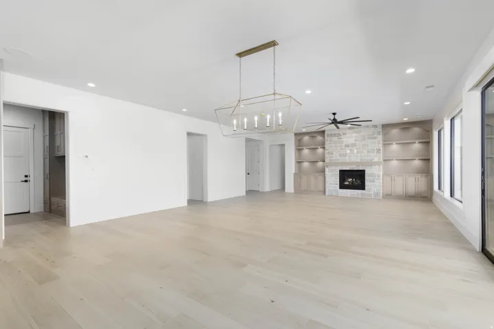 Vaulted ceilings, wood-finish flooring, stone fireplace, built-in cabinetry with shelving, and large windows