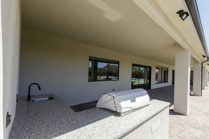 Covered patio featuring an outdoor kitchen with a built-in sink and granite-finish countertop, recessed lighting, and patio pavers