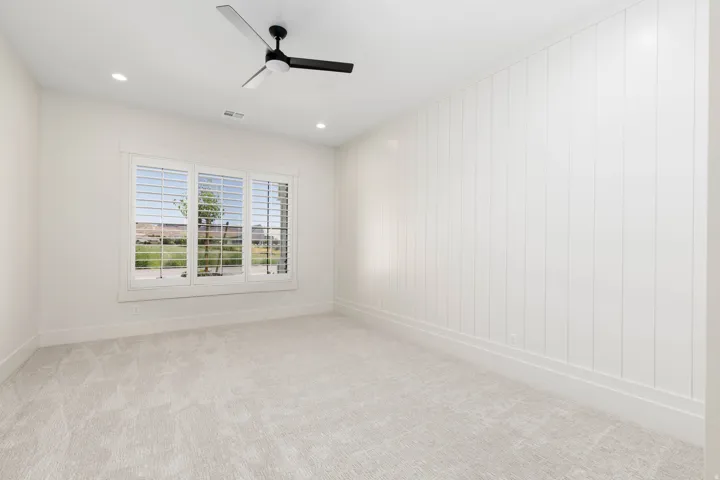 Carpeted room featuring a white paneled accent wall, a three-panel window with plantation shutters, recessed lighting, and a ceiling fan